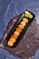 Wall Mural - Set of Baked Spicy Sushi on Black Plate with Ginger and Wasabi on Rock Surface