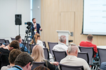 Wall Mural - business conference presentation with speaker, audience, and video camera recording session