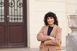 © Retamosa - A woman with curly hair is standing in front of a building with a brown door