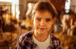 © Dasha Petrenko - A close-up portrait of a little girl in a plaid shirt on a farm. A cute child is smiling in the cowshed.