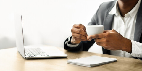 Poster - A businessman sits at a desk with a laptop and notebook, holding a white coffee cup.