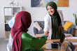 © Studio Marmellata - Two women shake hands in an office environment They are wearing hijabs and the atmosphere is professional and welcoming
