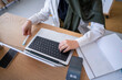 © Studio Marmellata - Close-up of a woman in a green hijab working on her laptop with a notebook beside her in a modern office This image emphasizes organization and productivity