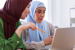 © Studio Marmellata - Two women in hijabs collaborate on a project in a modern office space One woman in a green hijab is smiling while the other in a blue hijab focuses on their work
