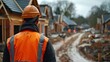 © Thanyaporn - An engineer supervises the construction of a new housing development wearing a reflective vest and helmet The background showcases the framework of several houses in progress The scene captures the