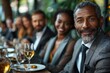 © DKPhoto - A diverse group of people dressed in smart attire smile and engage in conversation at a dinner table, capturing a moment of social connection and joy in a sophisticated setting.