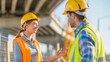 © Kiangdeb - Two construction workers wearing hard hats and safety vests engage in a conversation on a busy construction site
