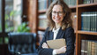 © Tetiana - A confident 50-year-old female lawyer with glasses holds a folder in her office against the backdrop of bookshelves and smiles softly, demonstrating professionalism and experience. copy space