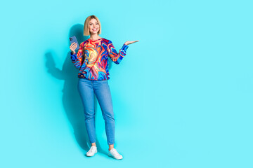 Wall Mural - Full length photo of attractive girl dressed print shirt holding smartphone arm show object empty space isolated on blue color background