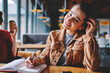 © BullRun - Portrait of positive smiling hipster girl writing essay with excited idea in notebook while female friend sitting near and enjoying coffee, happy woman looking at camera and doing homework indoors