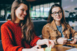 © BullRun - Smiling female designers studying together at university campus sitting at desktop with papers, happy positive women spending free time for learning indoors, concept of knowledge and education