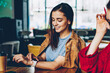 © BullRun - Positive hipster girl checking time and notification on contemporary smartwatch spending time with friend at cafeteria, two smiling women enjoying live conversation sitting at table in coffee shop