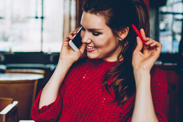 Wall Mural - Cheerful female student making positive telephone call using application for communication on smartphone in break of studying indoors while sitting near millennial friend concentrated on e learning