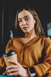 © BullRun - Portrait of concentrated clever female student spending time for autodidact with literature at coffee shop, serious woman looking at camera holding caffeine beverage and textbook foe education