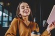 © BullRun - Portrait of successful smiling woman looking at camera and laughing holding caffeine beverage and notebook for knowledge, positive cheerful hipster girl enjoying literature and hobby at cafeteria