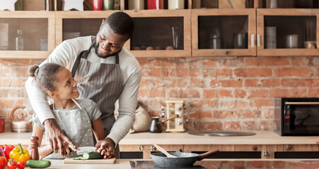 Wall Mural - Cheerful african father teaching daughter cutting veggies, cooking together at home, father and daughter, fatherhood concept, free space