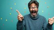 © Natalia - A cheerful middle-aged man with glasses and a beard pointing and laughing against a turquoise background with colorful confetti.