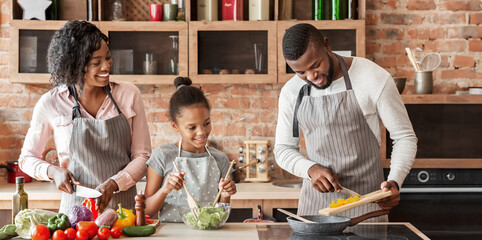 Wall Mural - African mom and daughter watching dad while cooking together at home, panorama with copy space