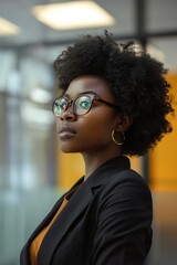 Poster - A woman wearing glasses and a black suit stands in front of a window. She looks confident and poised