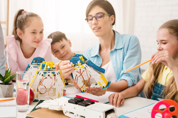 Aufkleber - A group of young students are learning about robotics and engineering in a classroom setting. A teacher is helping them build and program a robot, while they work together and ask questions.