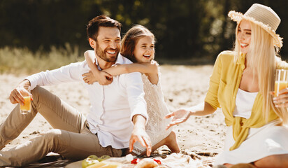 Wall Mural - Happy family enjoying picnic in nature, daughter hugging father and laughing