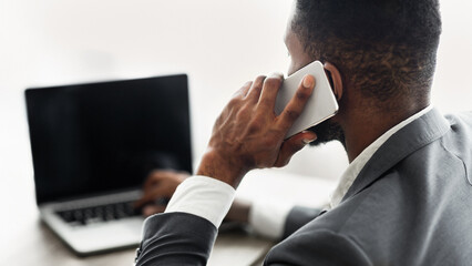 Poster - A businessman in a grey suit works on a laptop while talking on his cell phone.