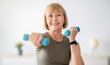 © Prostock-studio - Home training concept. Strong senior woman doing exercises with dumbbells indoors. Cheerful mature lady working out her arm muscles, keeping fit, leading healthy lifestyle during covid-19 isolation