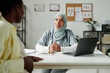 © pressmaster - Young female clinician in hijab listening to pregnant patient while sitting by workplace in front of laptop during medical consultation