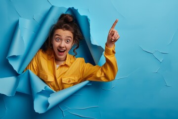 Young woman pointing to side through blue paper hole, solid background, happy and excited expression, professional photography.