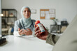 © pressmaster - Hand of young unrecognizable pregnant woman holding bottle of new vitamins while sitting in front of female gynecologist in hijab