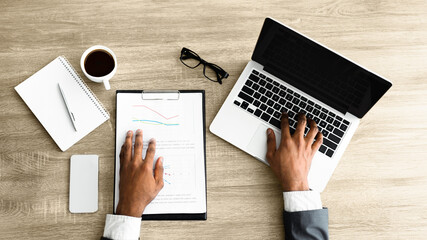 Poster - A businessman works on a laptop and reviews documents at his desk.