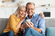 © Prostock-studio - Happy Senior Couple Using Smartphone Browsing Internet Together Sitting On Couch At Home And Hugging. Cellphone Users Use Mobile Application. Older Spouses Texting On Phone. Communication Concept