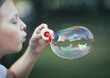 © jane_moss - A little girl blows a huge soap bubble in the park in the summer. Bokeh. Blonde, Caucasian. Close-up portrait.