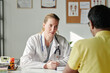 © pressmaster - Young female general practitioner in lab coat looking at male patient sitting in front of her and giving him medical advice