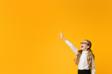 Wall Mural - Look There. Elementary School Girl Pointing Finger At Empty Space In Excitement Posing Over Yellow Studio Background.