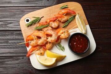 Wall Mural - Delicious grilled shrimp skewers served with sauce and lemon on wooden table, top view