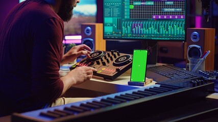 Wall Mural - Sound engineer working on mixing and mastering techniques in his home studio, using phone with greenscreen display while he is recording audio. Artist operating soundboard and amplifier. Camera A.