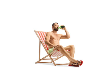 Wall Mural - Young man in swimwear drinking beer seated in a beach chair