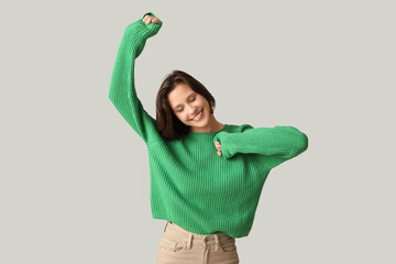 Wall Mural - Happy young woman in stylish green sweater on grey background