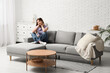 © Pixel-Shot - Pretty young woman sitting on comfortable sofa in living room