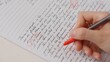 © kinomaster - Professional school or college teacher grades a homework exam papers of students. Woman checks essay, crosses wrong words, corrects it with red pen.