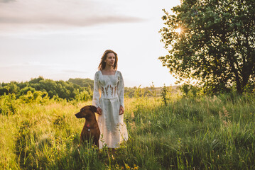 young cheerful woman playing with her dog outdoors in beautiful countryside field. Female and ridgeback dog walking and having fun