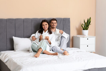 Poster - Happy young couple with cups of coffee sitting in bedroom