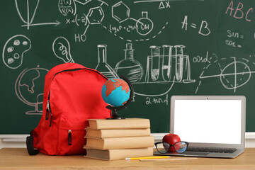 Wall Mural - School desk with backpack, globe, books and laptop in light classroom