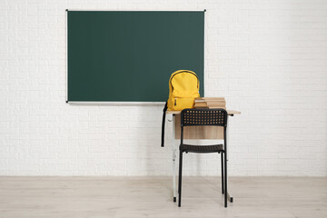 Sticker - School desk with backpack, books and blackboard on white brick wall in light classroom