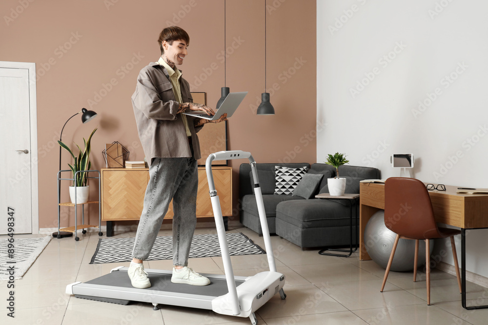 Young man using laptop on treadmill in office
