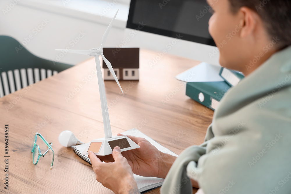 Male engineer with wind turbine model at table in office, closeup