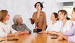 © JackF - In classroom, students sit at common round table and animatedly discuss plans for field practice outside city. Young woman student activist stands at table and leads joint discussion