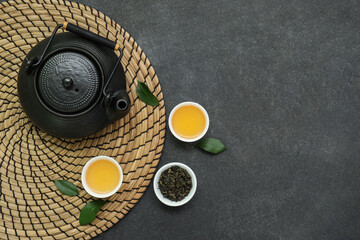 Bowls and teapot of hot tea with dried leaves on black background