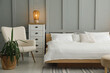 © New Africa - Stylish bedroom interior with comfortable bed, lamp, armchair and houseplant